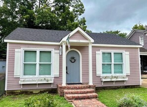 A single-story house with a front entrance, two windows with shutters, and a small porch with steps.