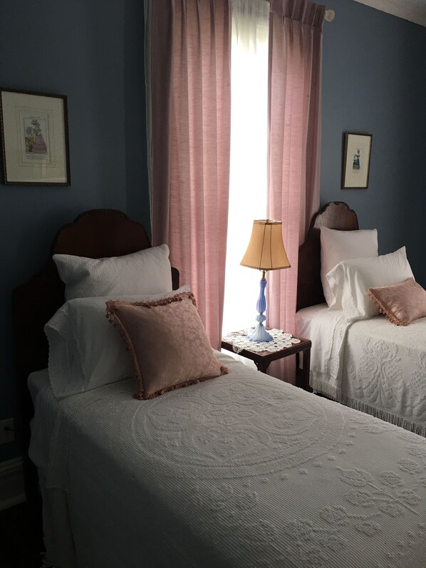 A bedroom with two beds, a nightstand, a lamp, and a window with curtains. - The Wynne House Inn (Holly Springs)