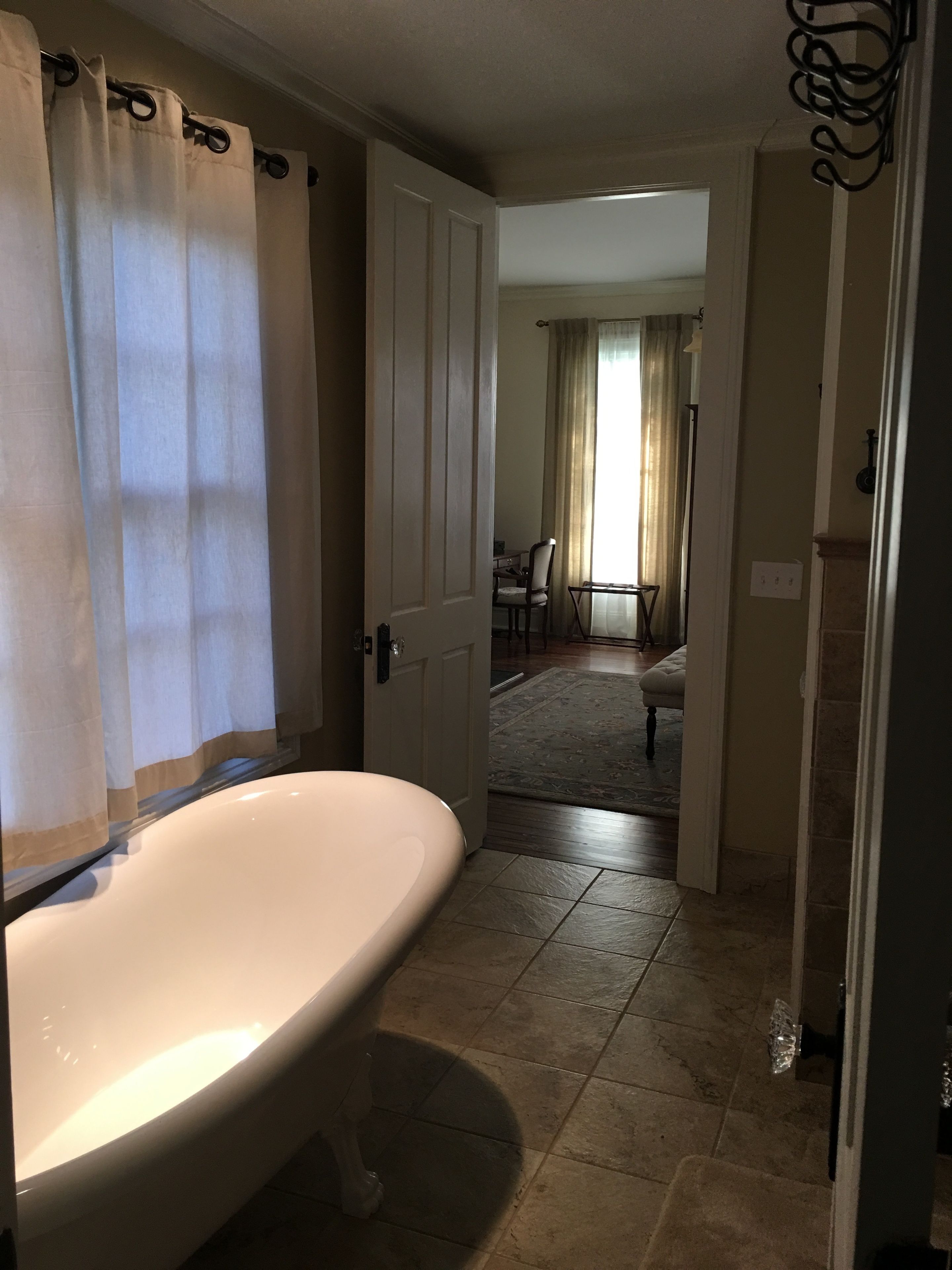 A bathroom with a freestanding bathtub, a door leading to a dining area, and a rug on the floor.