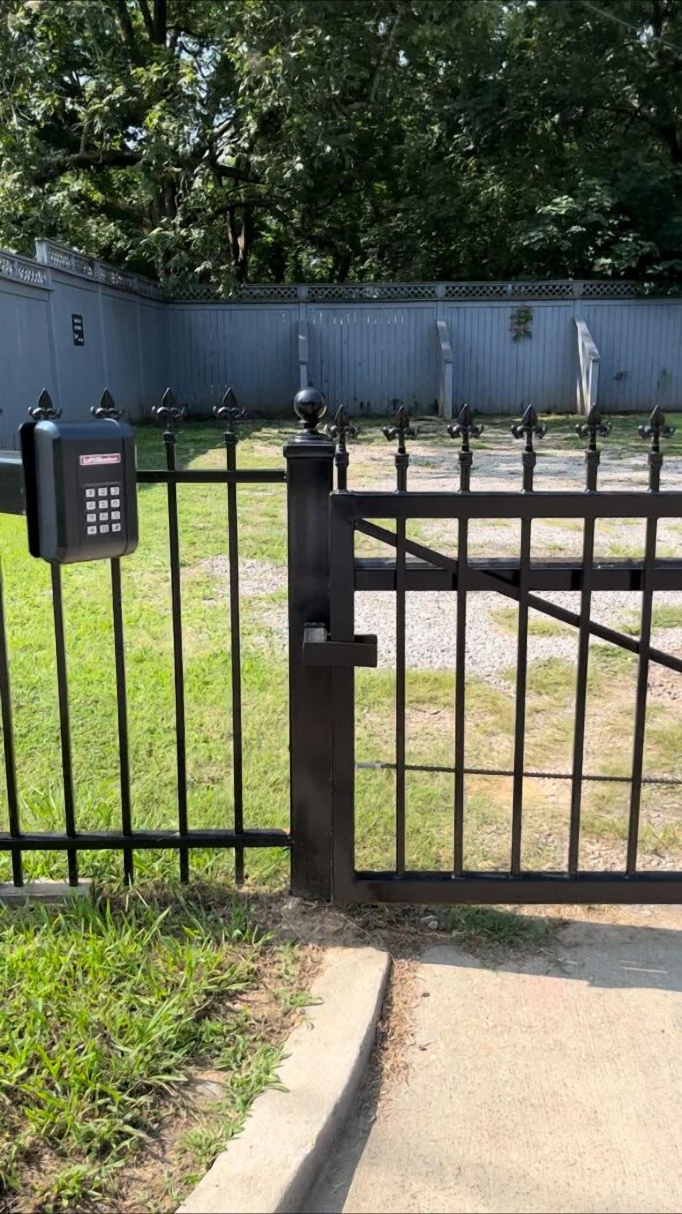 A gated entrance with a keypad lock, a metal gate, and a concrete pathway.