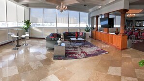 A spacious living area with a large window, a sofa, a coffee table, and a bar area with a TV. - Intracostal Sunny Isles (Sunny Isles Beach)