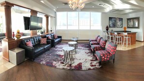 A spacious living room with a black leather sofa, red patterned chairs, a round coffee table, and a large window offering a city view. - Intracostal Sunny Isles (Sunny Isles Beach)