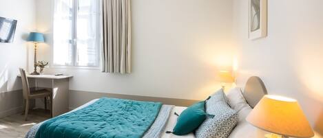 Un dormitorio con cama, lámparas de noche, escritorio y una silla.