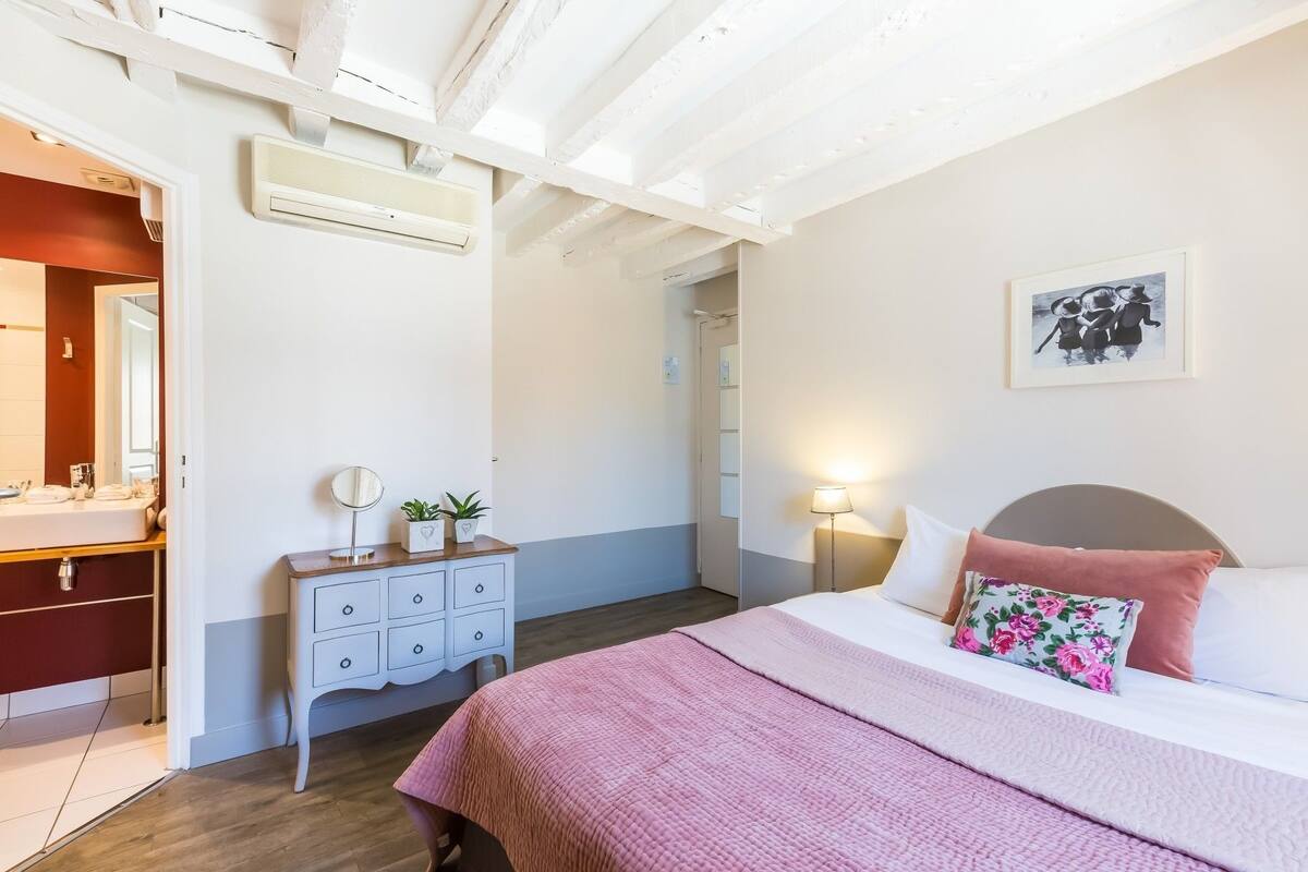 Une chambre à coucher avec un lit, une table de chevet et un miroir. Une porte donne accès à une autre pièce.