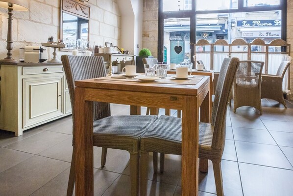 A dining area with a wooden table and wicker chairs, a white cabinet, and a window with a view of the street.