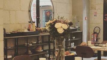 A dining area with round tables, chairs, and a vase with flowers. There is a mirror on the wall and shelves with various items.