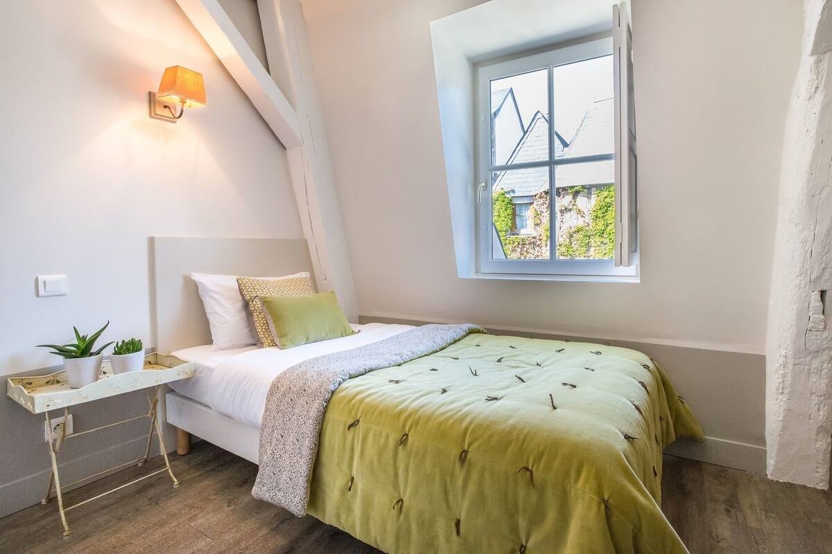Une chambre à coucher avec un lit, une table de chevet agrémentée de plantes, une fenêtre donnant sur un paysage agréable et un luminaire fixé au mur.