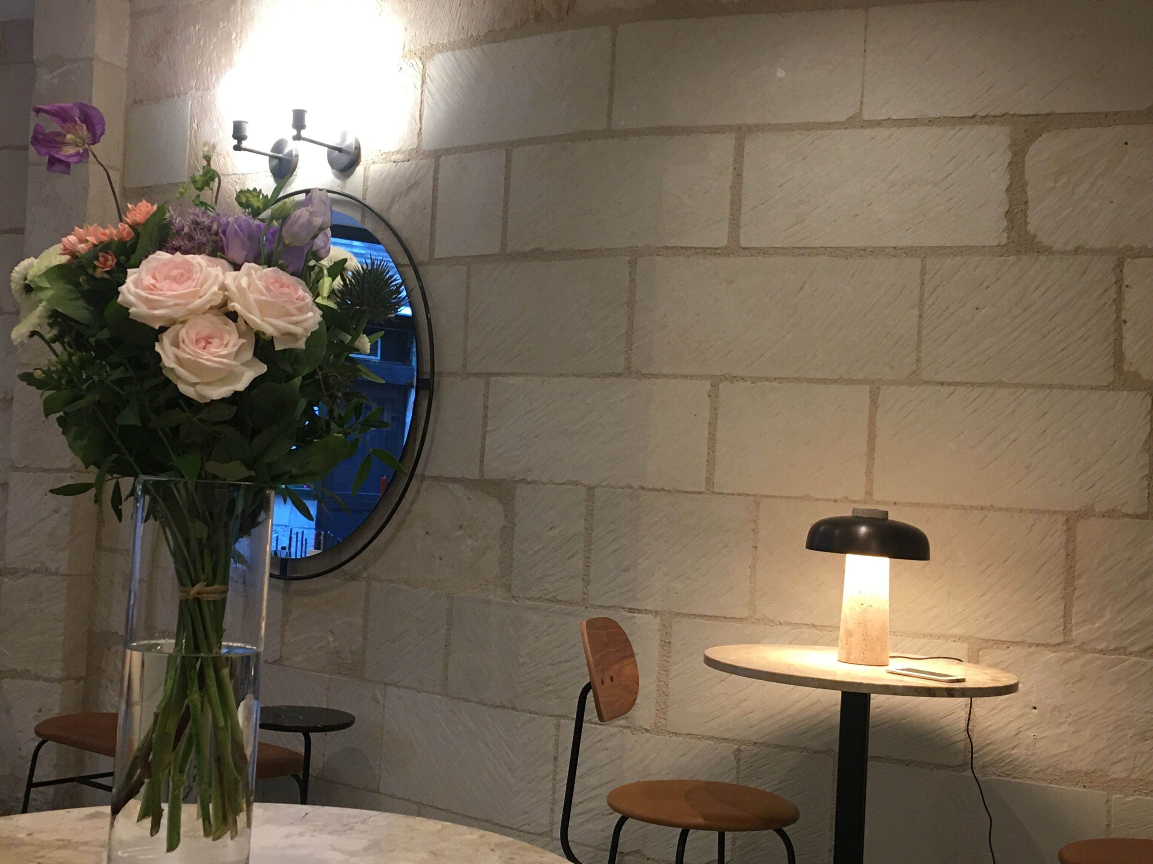 Une table avec un vase de fleurs, une lampe et des chaises, dans une pièce aux murs en pierre.
