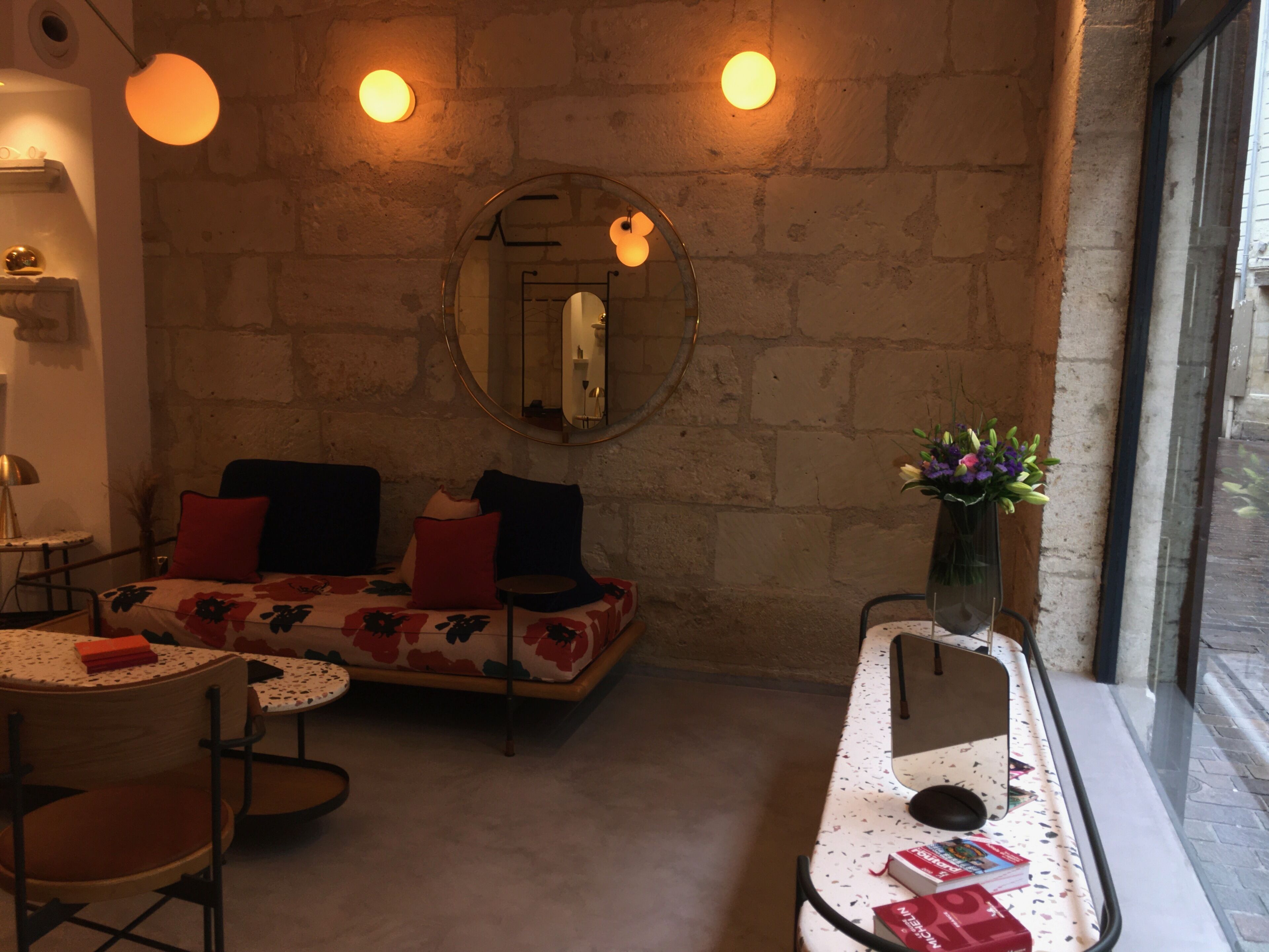 Una habitación acogedora con un sofá, una mesita, un espejo y un jarrón con flores.