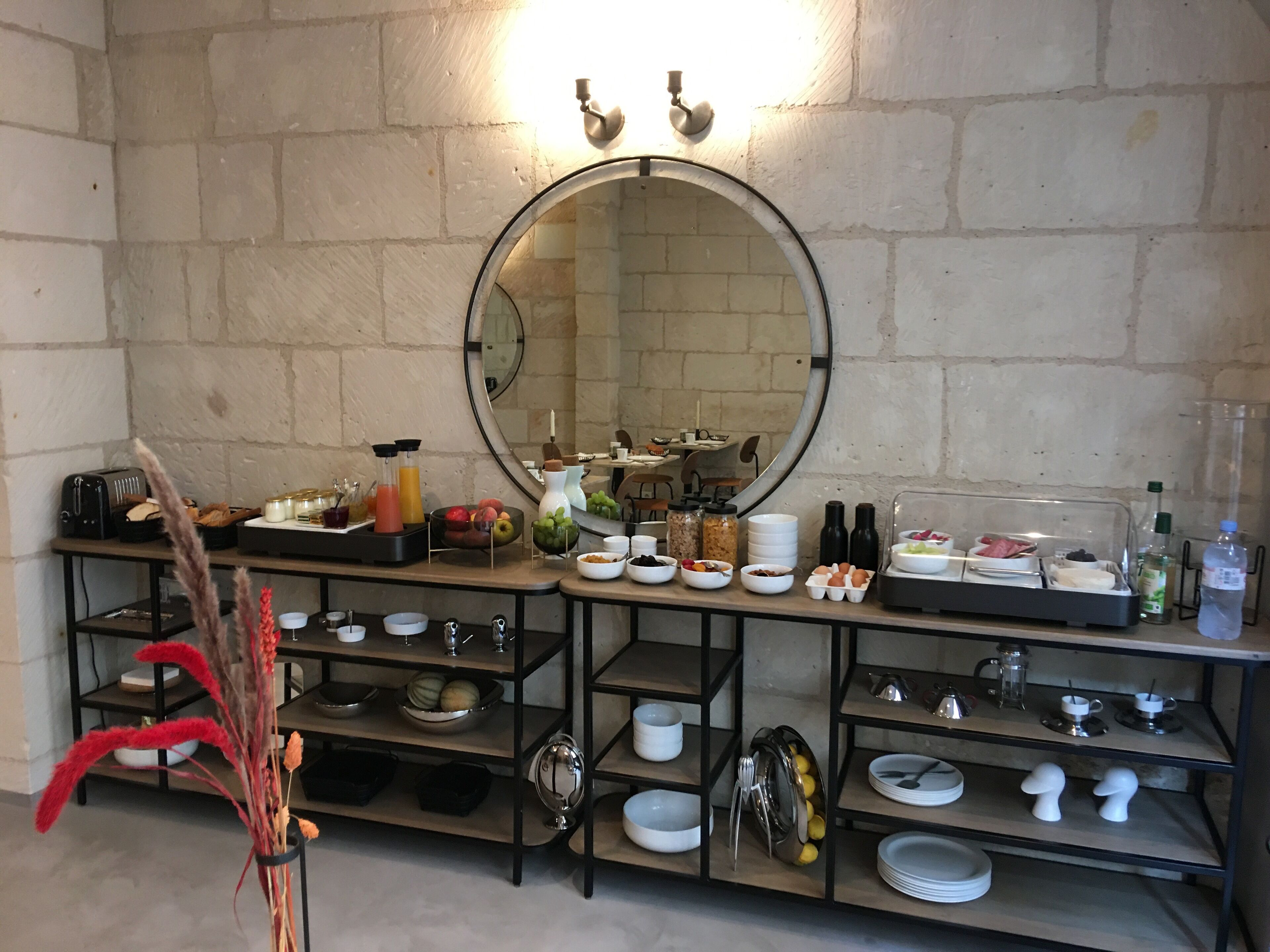 A breakfast buffet setup with various food items and beverages, a mirror, and a decorative plant.