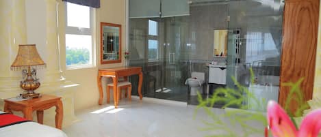 Habitación de hotel con un gran ventanal corredero que da a un balcón, una mesa de madera con una silla, una lámpara y una cama.