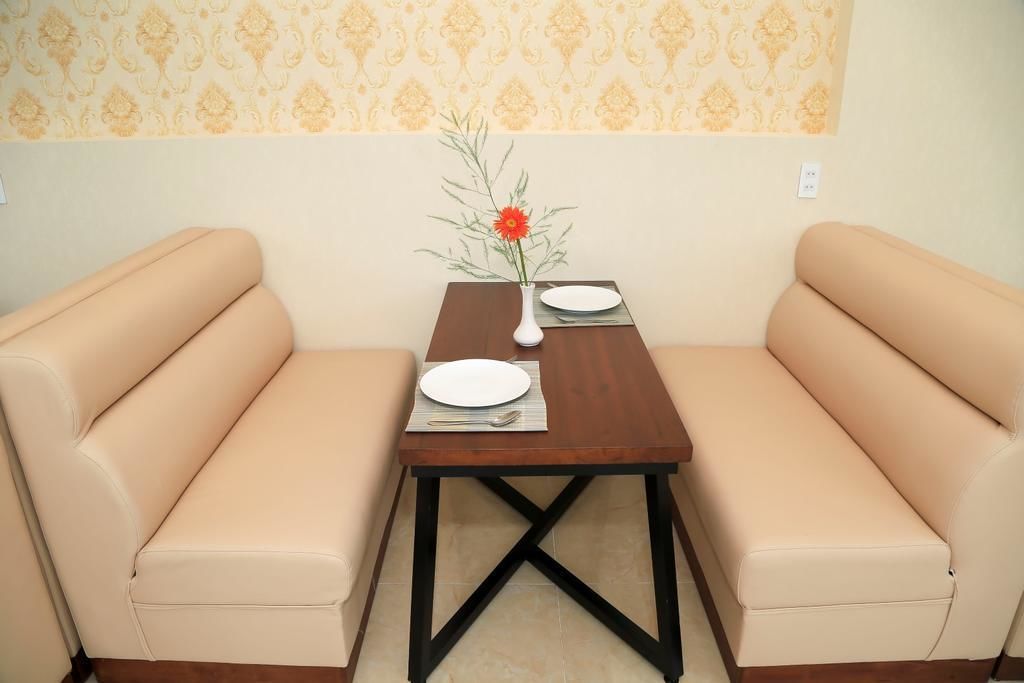 A dining area with two beige sofas, a wooden table with a vase of flowers, and a patterned wallpaper background.