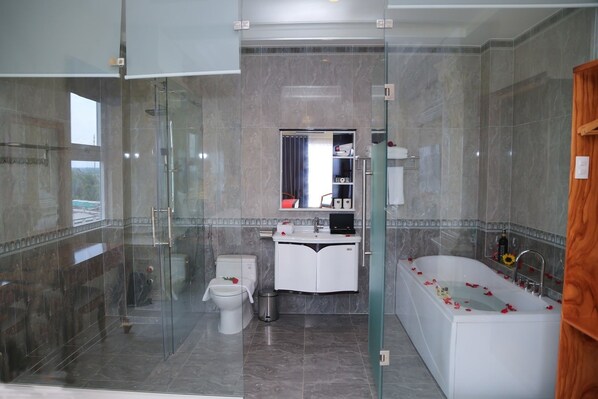 A modern bathroom with a glass-enclosed shower, a white toilet, a vanity with a sink, and a bathtub with rose petals. - Van Kim Long (Tan Duong)