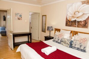 A hotel room with a bed, a desk, a chair, a door, and a painting. - Goulden Street Guest House (East London)