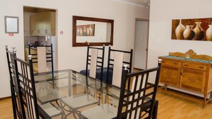 A dining area with a glass table, black chairs, a wooden cabinet, and a painting on the wall. - Goulden Street Guest House (East London)