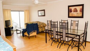 A room with a bed, a TV, a dining table with chairs, a ceiling fan, and a painting on the wall. - Goulden Street Guest House (East London)
