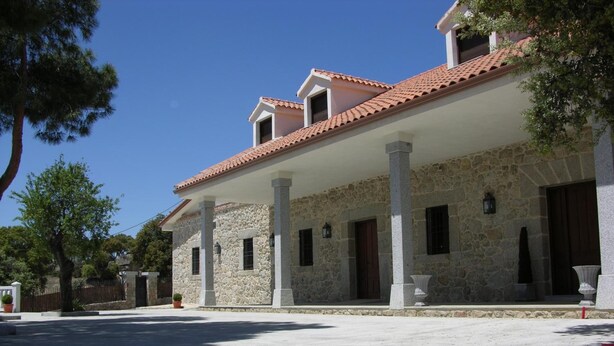 A stone building with a tiled roof, columns, and a covered patio area.