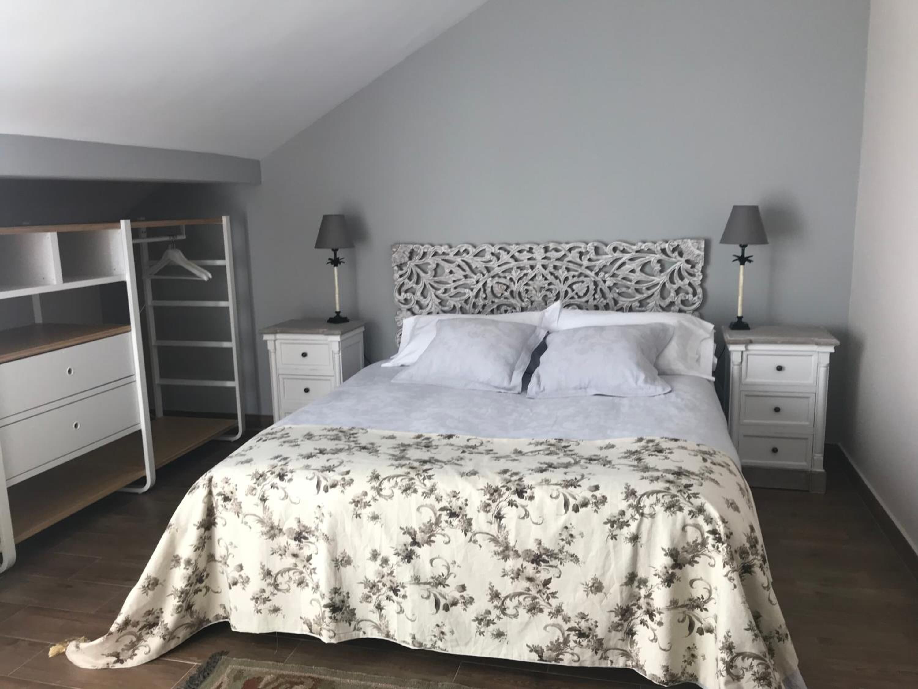 A bedroom with a bed, nightstands, a wardrobe, and a decorative headboard.