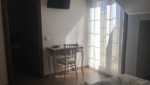A room with a bed, a desk with a chair, a TV on the wall, and a window with curtains.