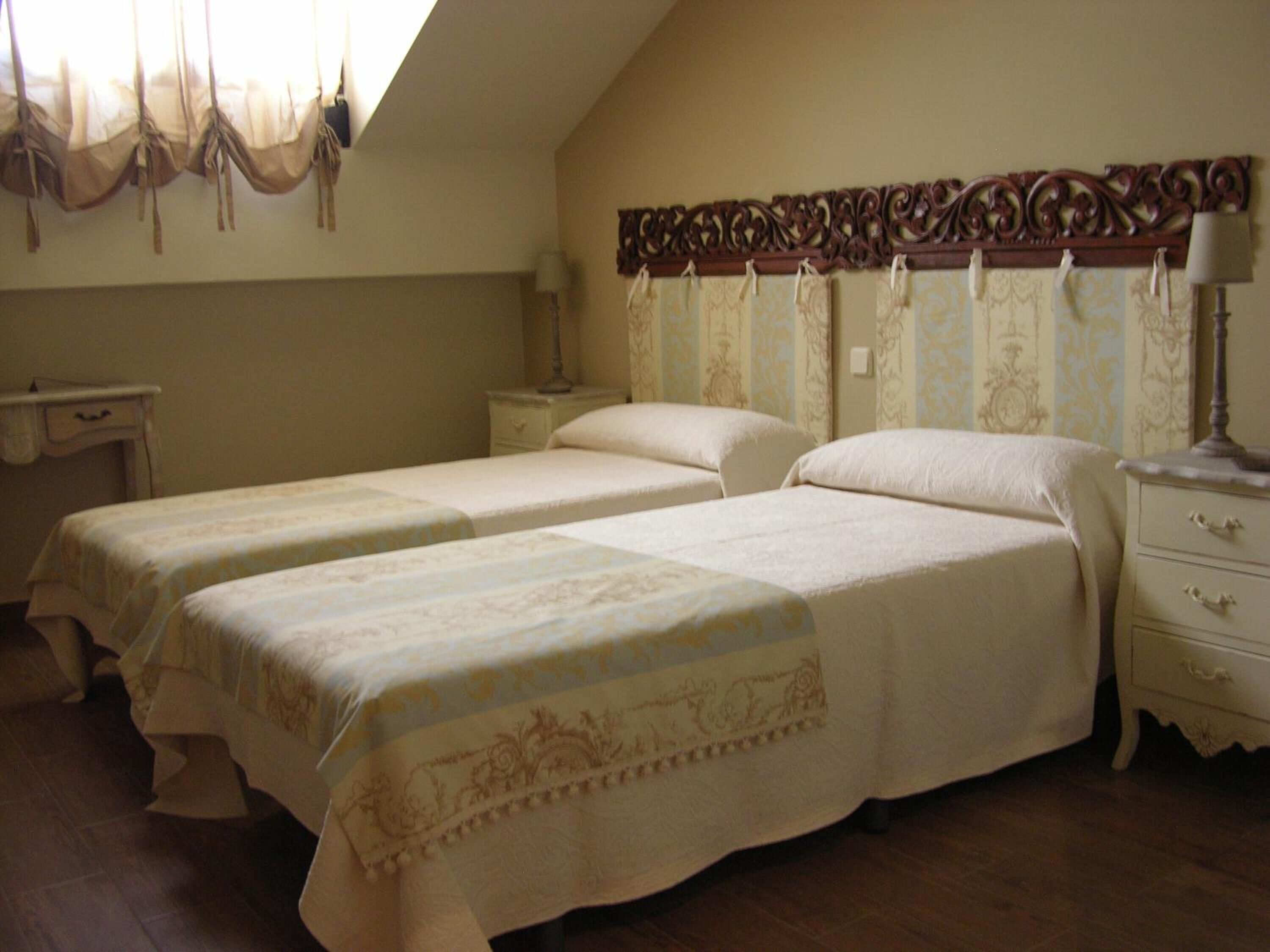A bedroom with two single beds, a nightstand with a lamp, a dresser, and a decorative headboard.