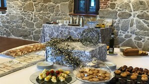 A buffet table with various food items, including pastries, cookies, and fruit skewers, set against a stone wall backdrop.