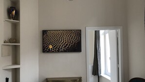 A room with a white wall, a black and gold artwork, a patterned curtain, a small table, and a chair. - Exclusive Flats In Brussels - Olives (Brussels)