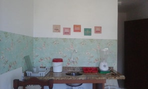 A kitchen with a blender, a sink, and a floral backsplash. There are four small signs on the wall. - Quarto e sala (Ilhéus)