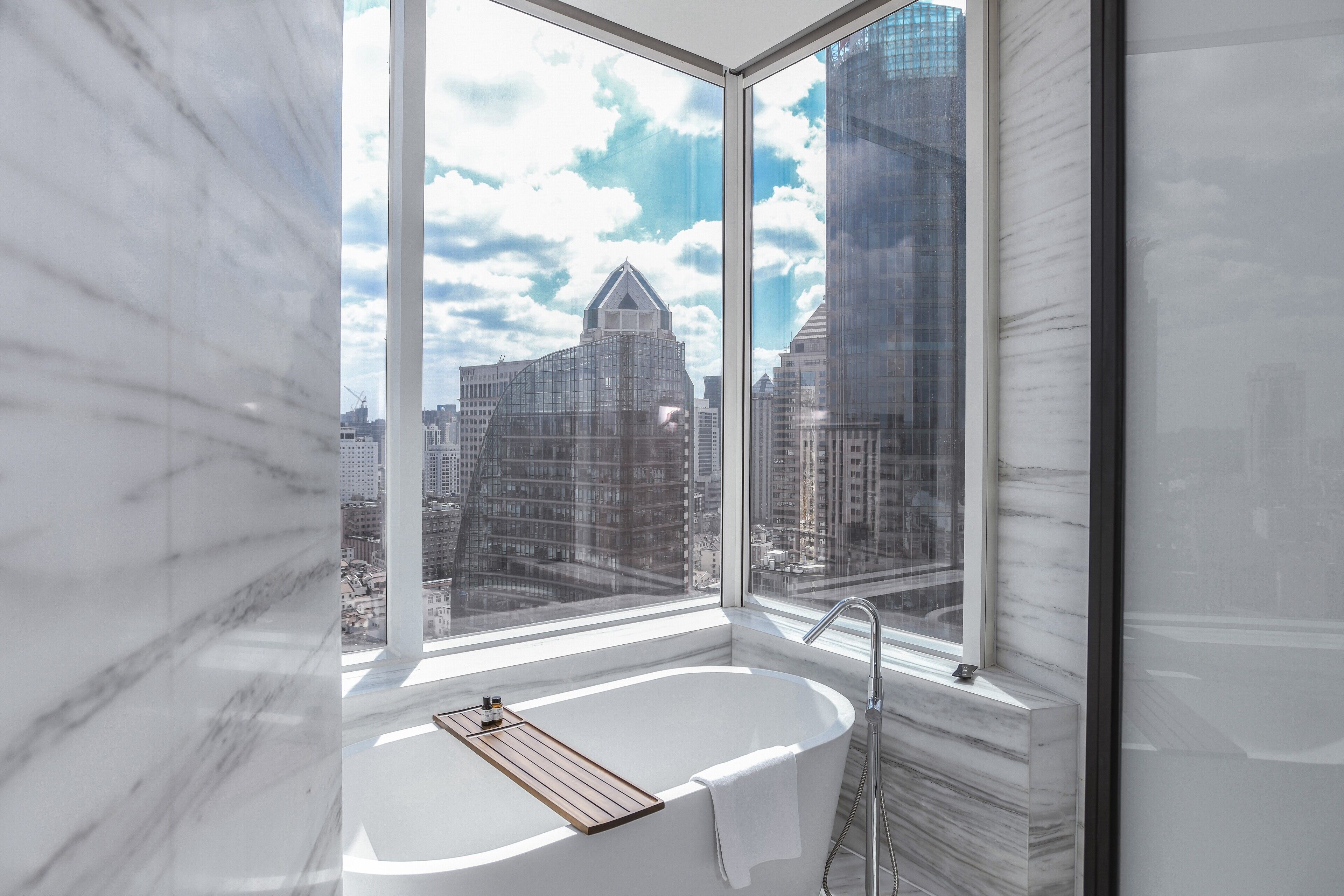 A modern bathroom with a large window, a bathtub, and a marble wall.