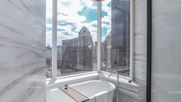 A modern bathroom with a large window, a bathtub, and a marble wall.