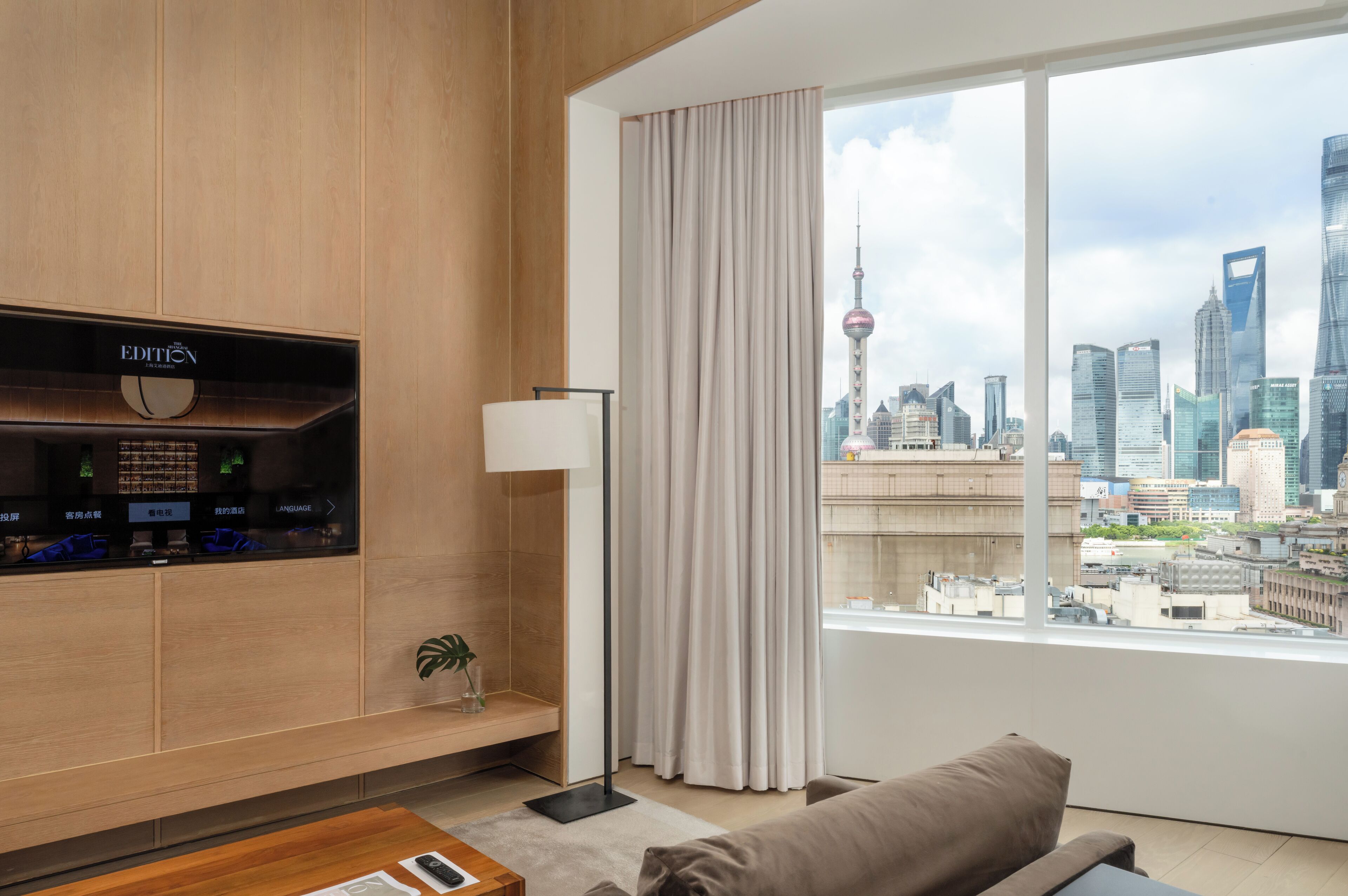Een moderne hotelkamer met een groot raam met uitzicht op de skyline van de stad, een flatscreen televisie aan de muur en een comfortabele zithoek.