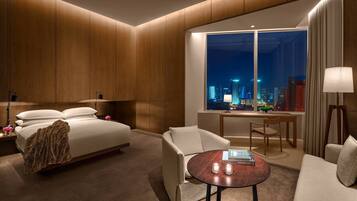 Habitación de hotel con cama, dos sillones, una mesita, escritorio y un ventanal con vista a la ciudad.
