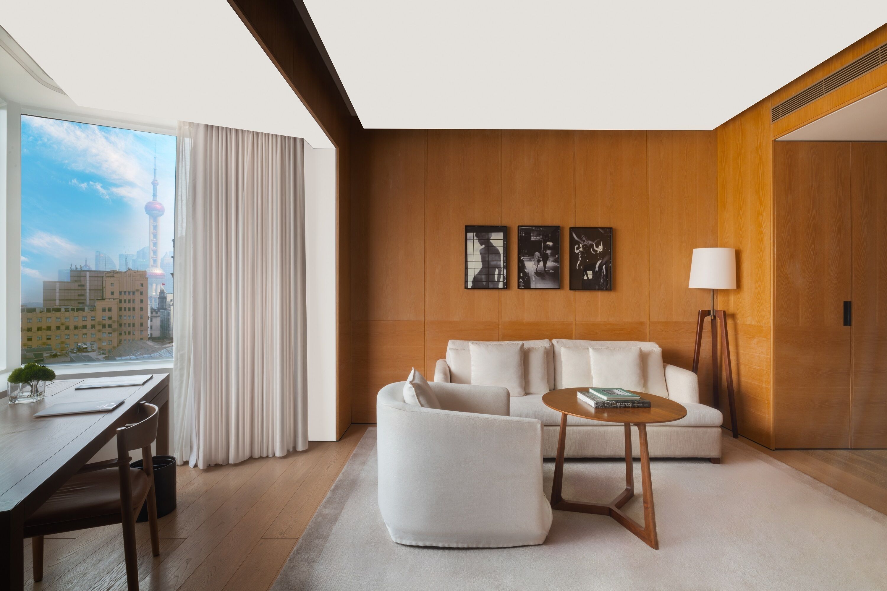 A modern living room with a sofa, coffee table, and lamp, a dining area with a table and chairs, and a large window with a view of a cityscape.