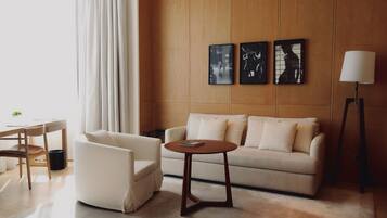 Una sala de estar moderna con un sofá, un sillón y una mesa de centro redonda. Hay tres cuadros enmarcados en la pared, una lámpara de pie y una ventana con cortinas.