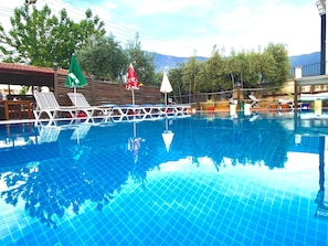 A swimming pool with lounge chairs and umbrellas, surrounded by trees and a mountain view.