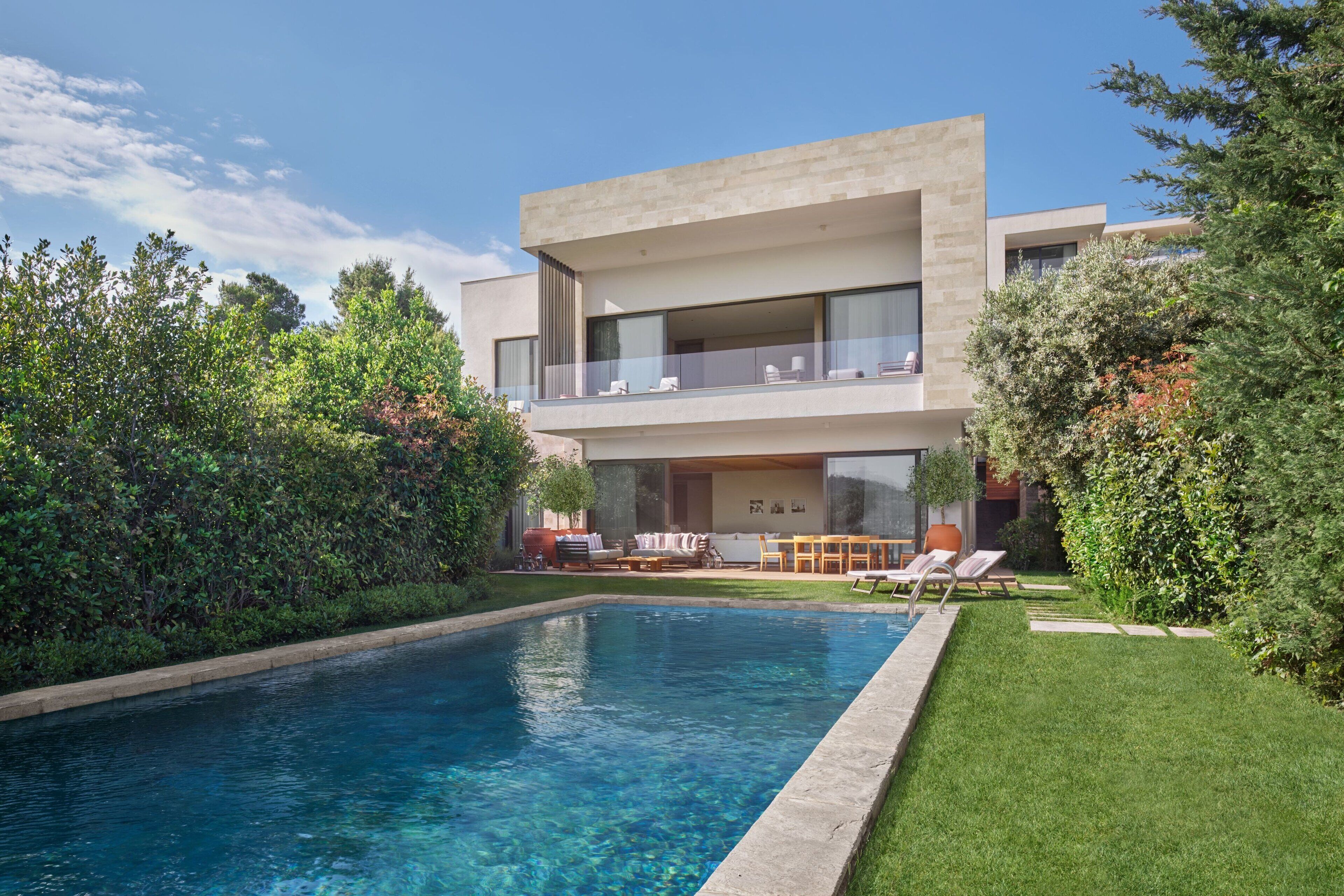 A modern two-story house with a swimming pool, outdoor furniture, and lush greenery.