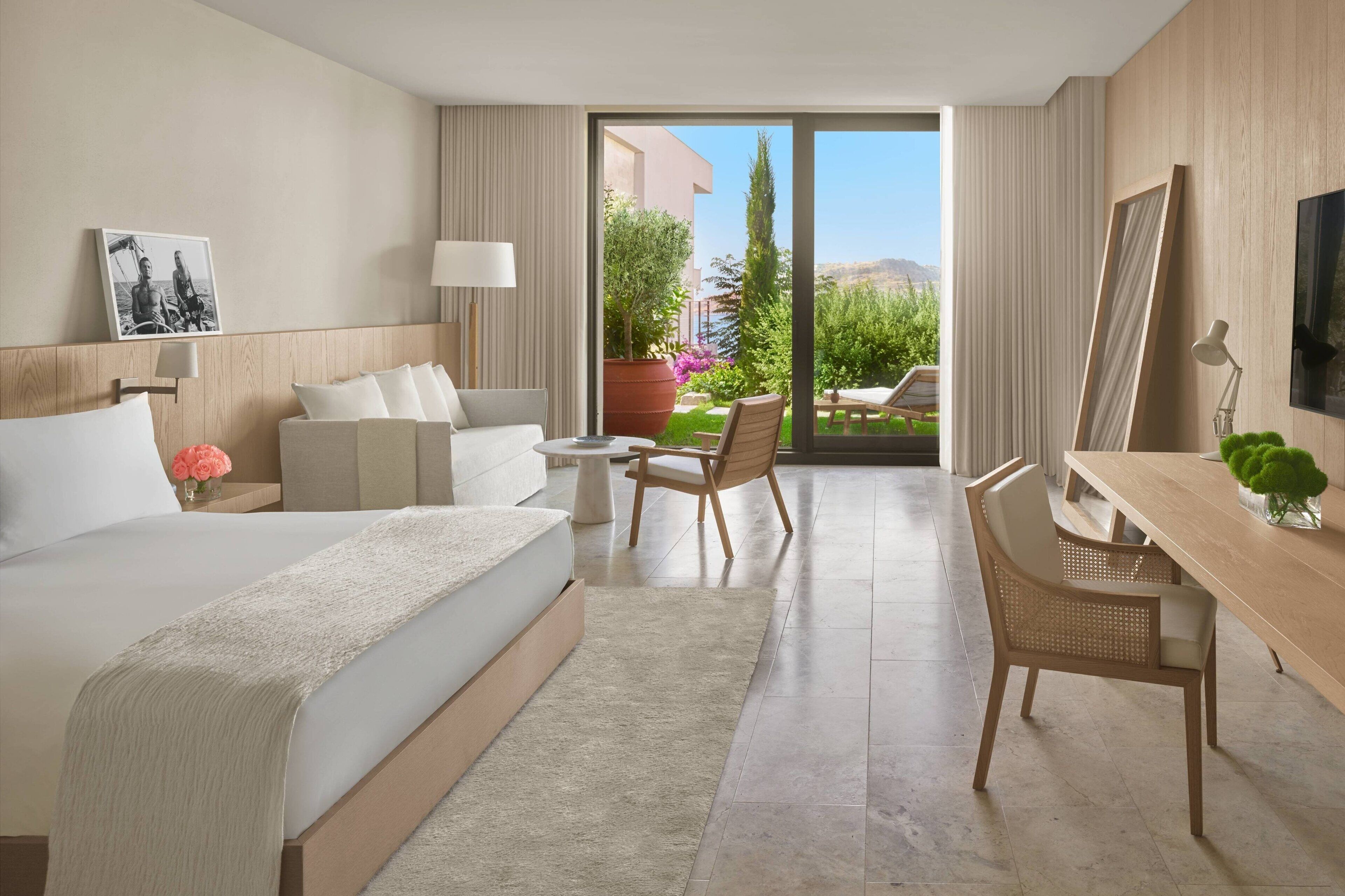 Habitación de hotel con cama, escritorio, silla, una mesita y vistas al exterior.