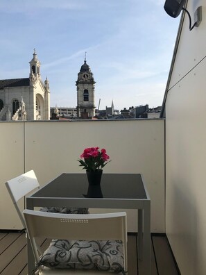 A balcony with a table and chairs, a potted plant, and a view of a historic building with a clock tower. - Exclusive Flats Sainte-Catherine Terrace (Brussels)