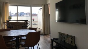 Ein modernes Wohnzimmer mit einem runden Esstisch, bequemen Sitzgelegenheiten, einem flachbildfernseher an der Wand und einem Balkon mit Blick auf die Stadt.