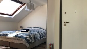 Ein Schlafzimmer mit Dachfenster, einem Bett mit gemusterten Betttextilien, einer Nachttischlampe und einer Tür mit Schlüsselloch.
