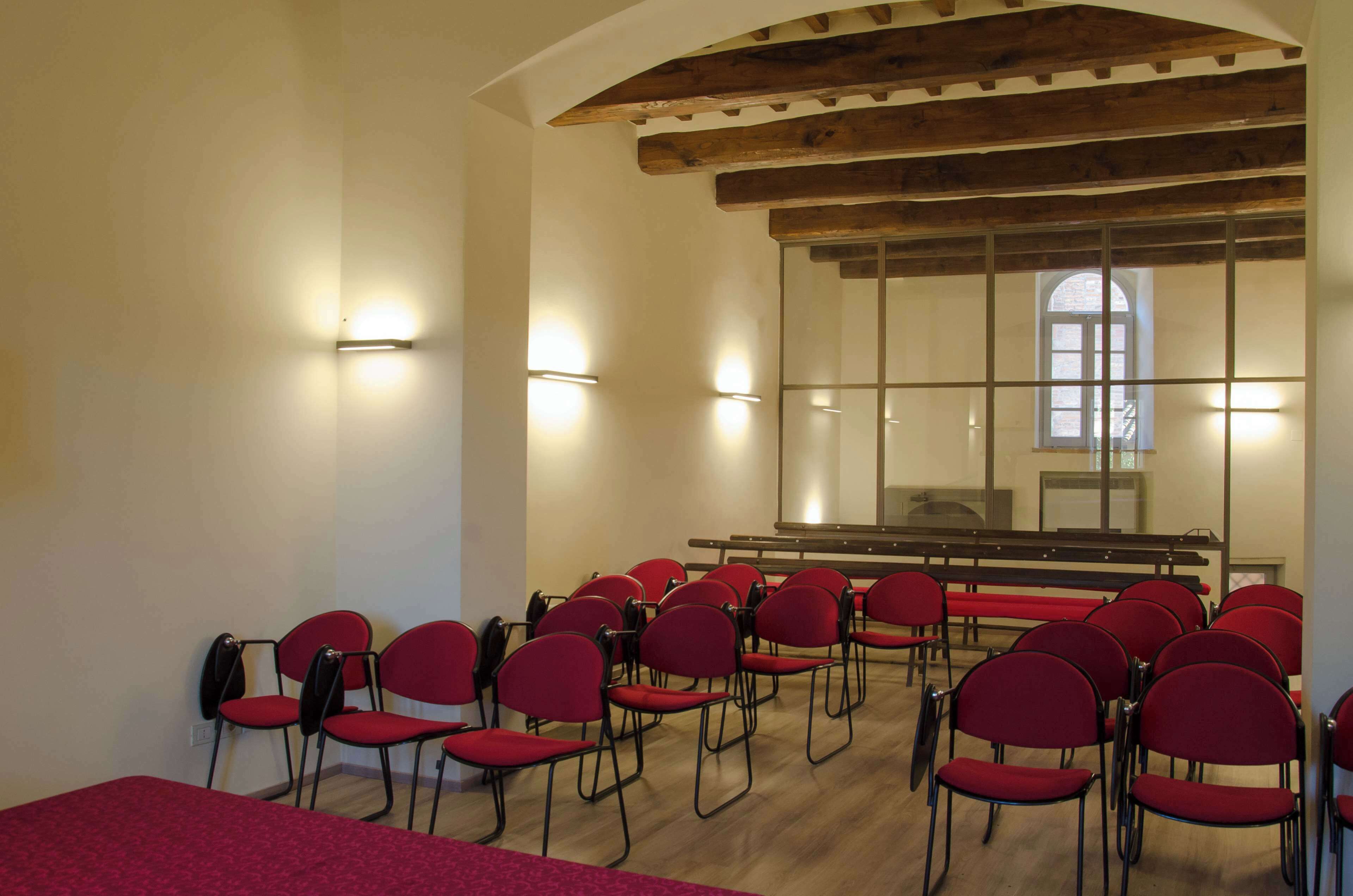 A conference room with red chairs arranged in rows, wooden beams on the ceiling, and a large window with a view.