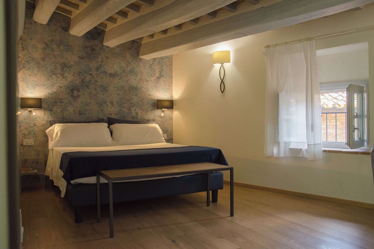Ein Schlafzimmer mit einem Bett, Nachttischlampen, einer Bank und einem Fenster mit Vorhängen.