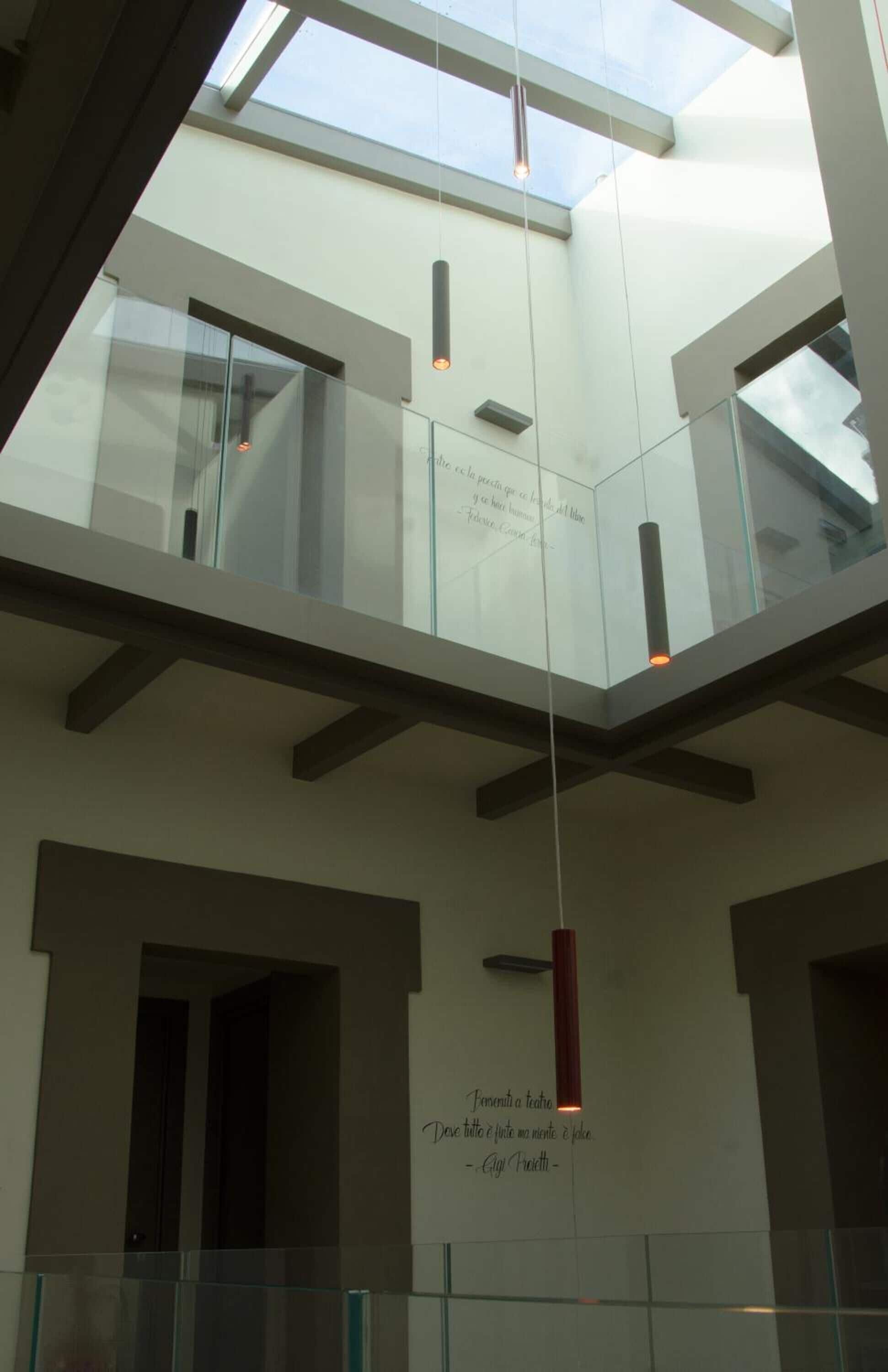 Un intérieur moderne avec un plafond en verre, un luminaire suspendu rouge et une citation inspirante sur le mur.