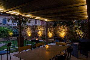 Eine Terrassenfläche im Freien mit Tischen und Stühlen, Steinmauern und einer Holzpergola.
