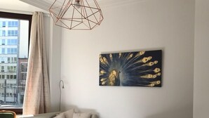 A bedroom with a bed, a chair, a table, a peacock painting, and a geometric pendant light. - Exclusive Flats Sainte-Catherine Art (Brussels)