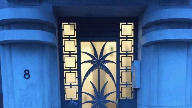 A building entrance with a dark door featuring a palm tree design and numbered panels. - Exclusive Flats Sainte-Catherine Art (Brussels)