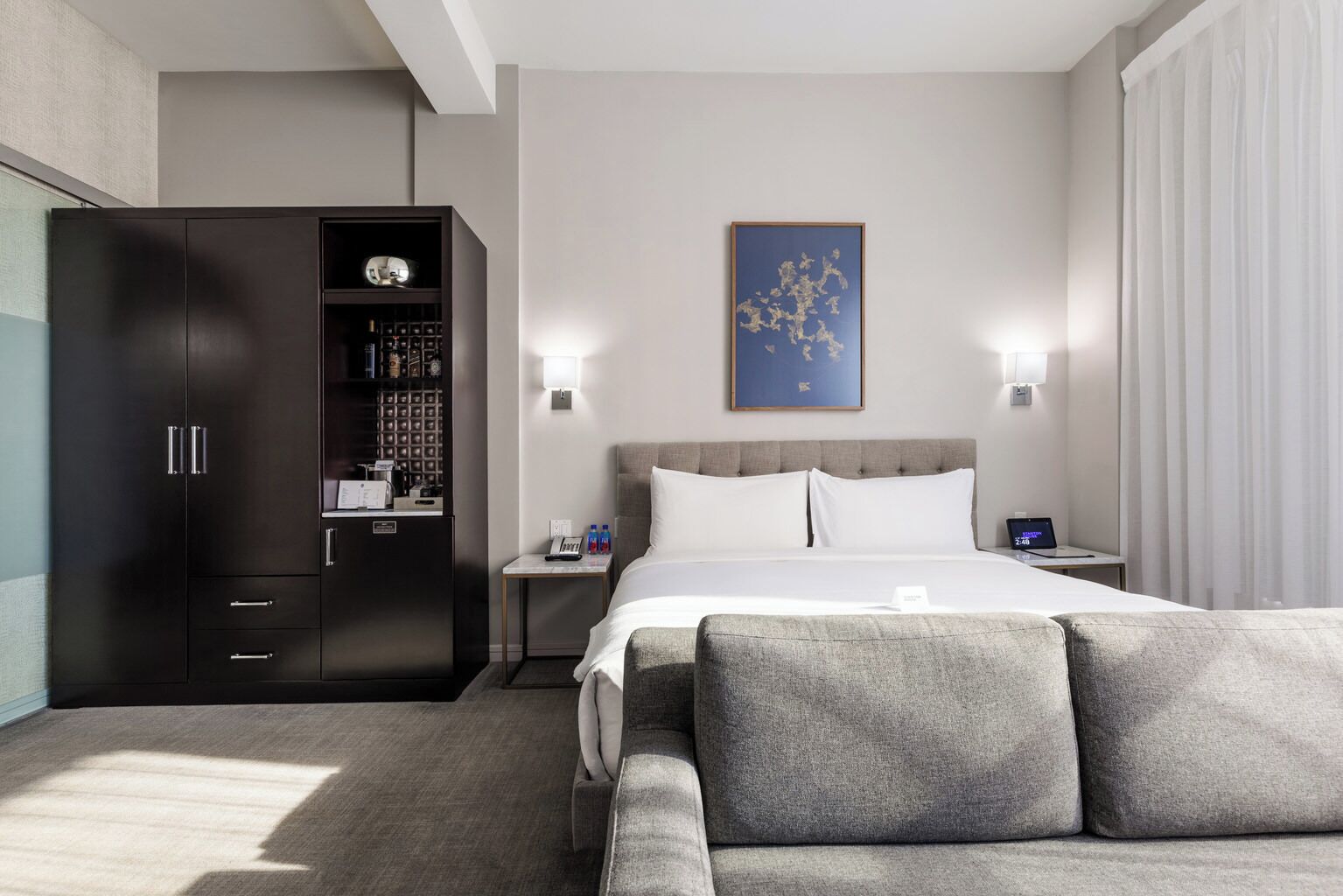 A modern hotel room with a large bed, a wardrobe, a small table, and a wall-mounted artwork.