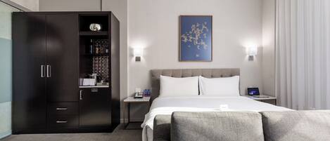 A modern hotel room with a large bed, a wardrobe, a small table, and a wall-mounted artwork.