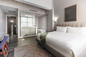 A modern hotel room with a large bed, a bathroom with a bathtub, a desk, and a chair.