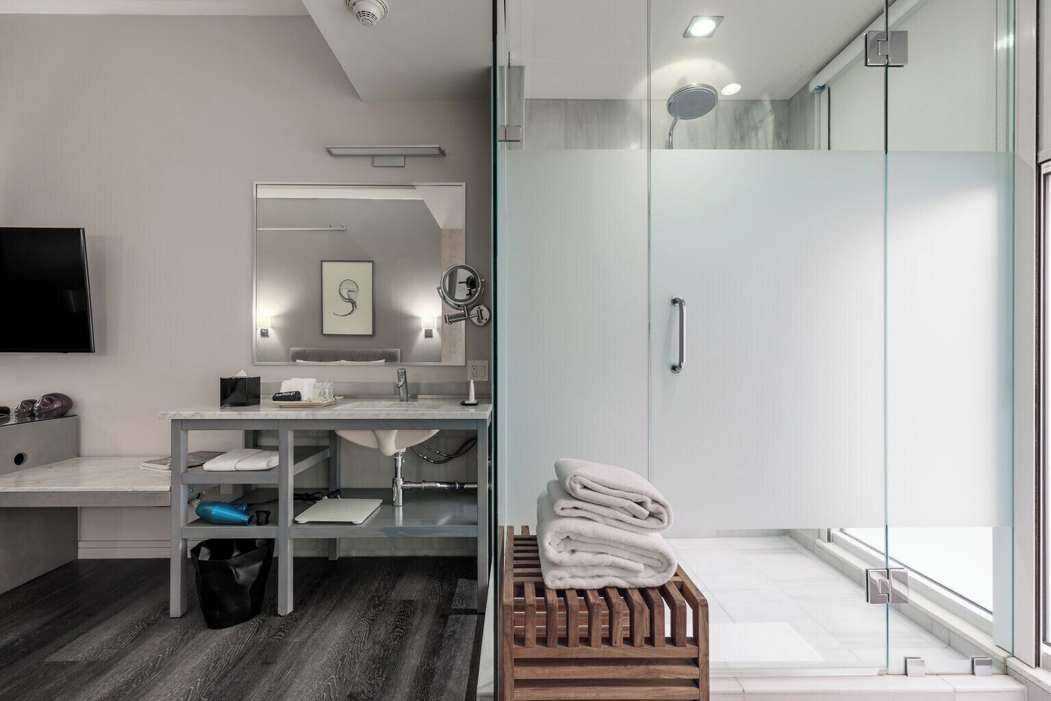 A modern bathroom with a glass shower enclosure, a vanity with a mirror, and a wooden bench with towels.