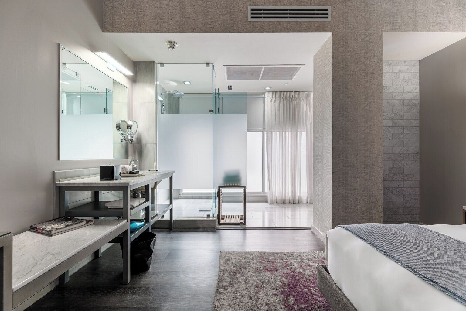 Een moderne hotelkamer met een groot bed, een kaptafel met spiegel, een douche en uitzicht op de stad.